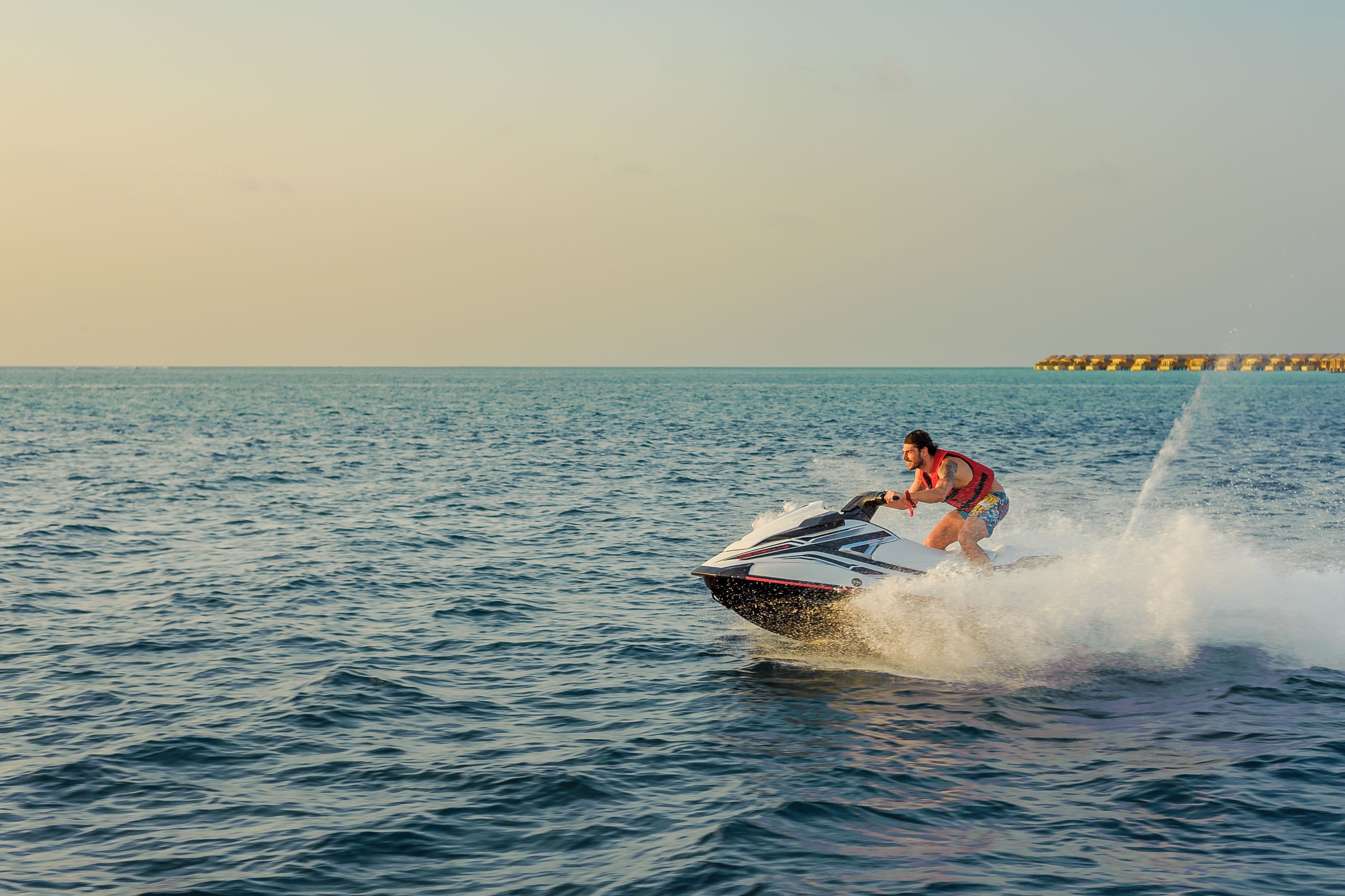 A rider on a jet ski kicking up spray at sunset, with overwater villas in the distance