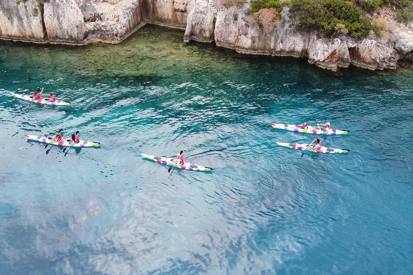 A group of kayakers paddling through turquoise water beside a rocky coastline