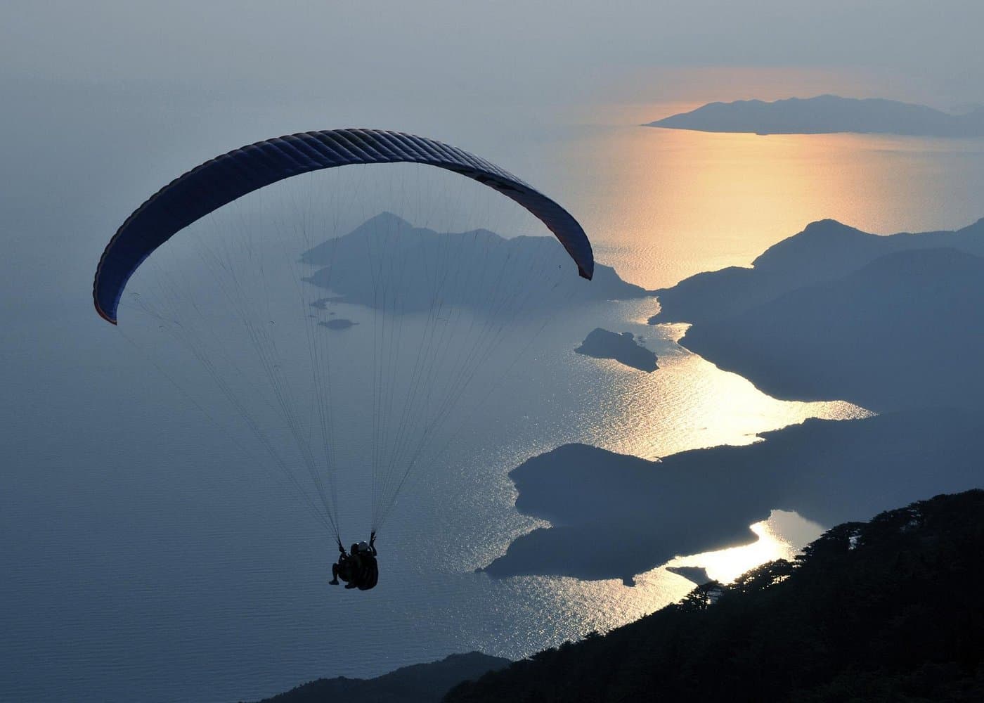 A paraglider silhouetted above the coastline at sunset, with islands and bays visible below