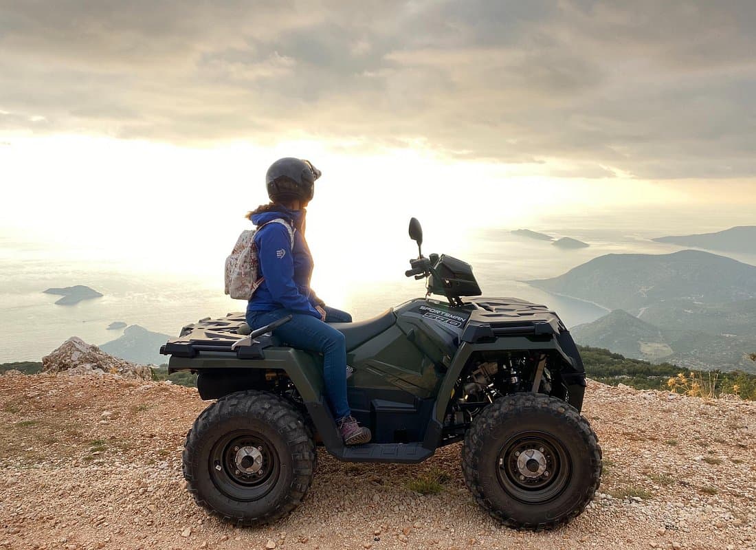 A quad bike rider pausing on a mountain ridge overlooking the Mediterranean coastline