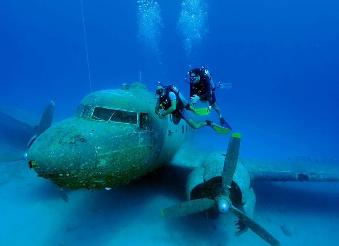 Two scuba divers exploring a sunken aircraft wreck underwater