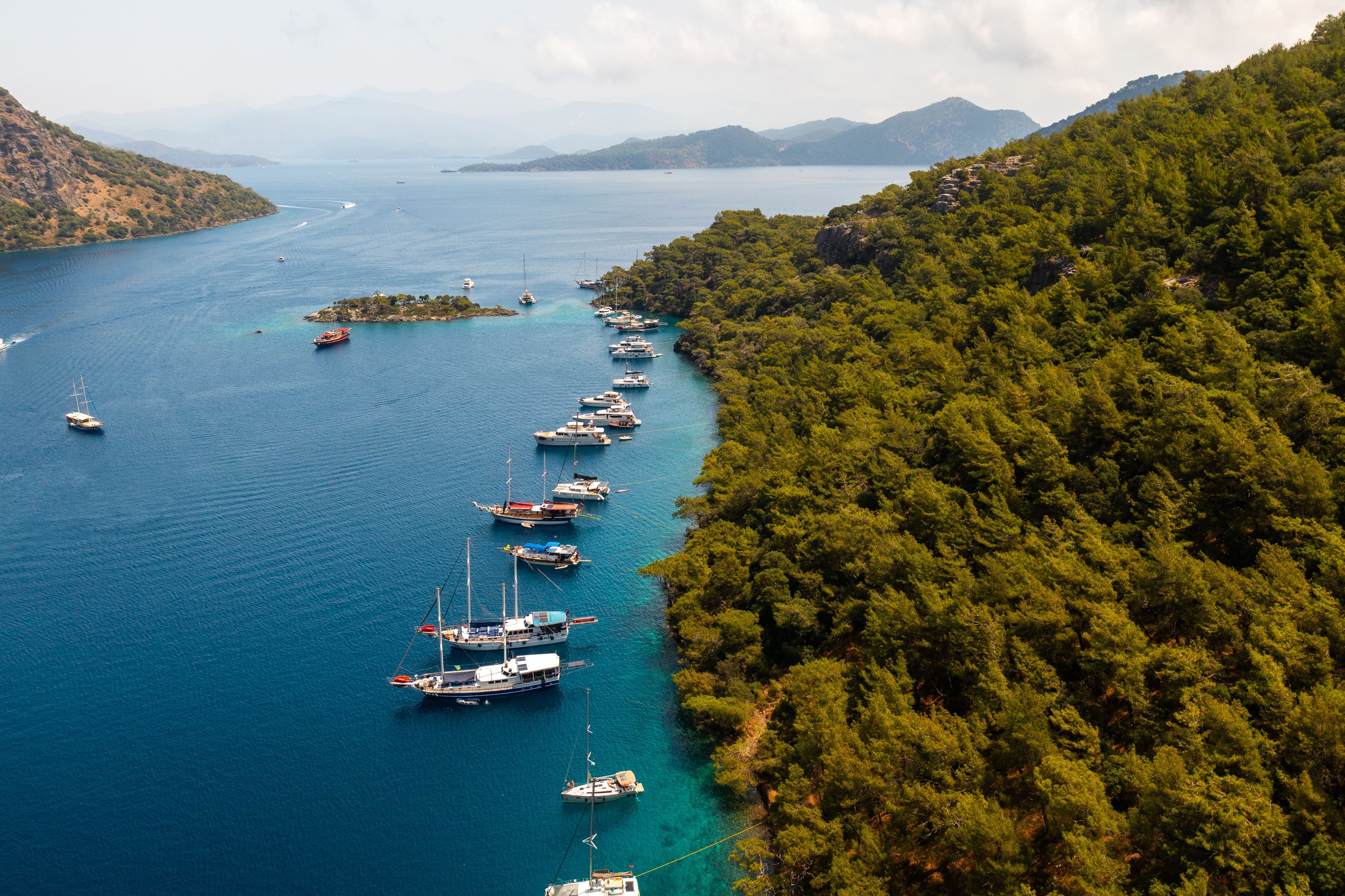 An aerial view of yachts and gulets anchored along a forested bay near Göcek