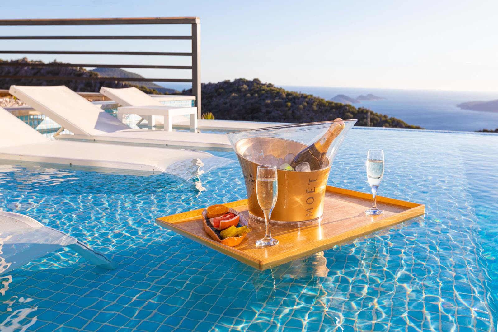 A floating tray with a champagne bucket and two glasses in an infinity pool, overlooking the coast