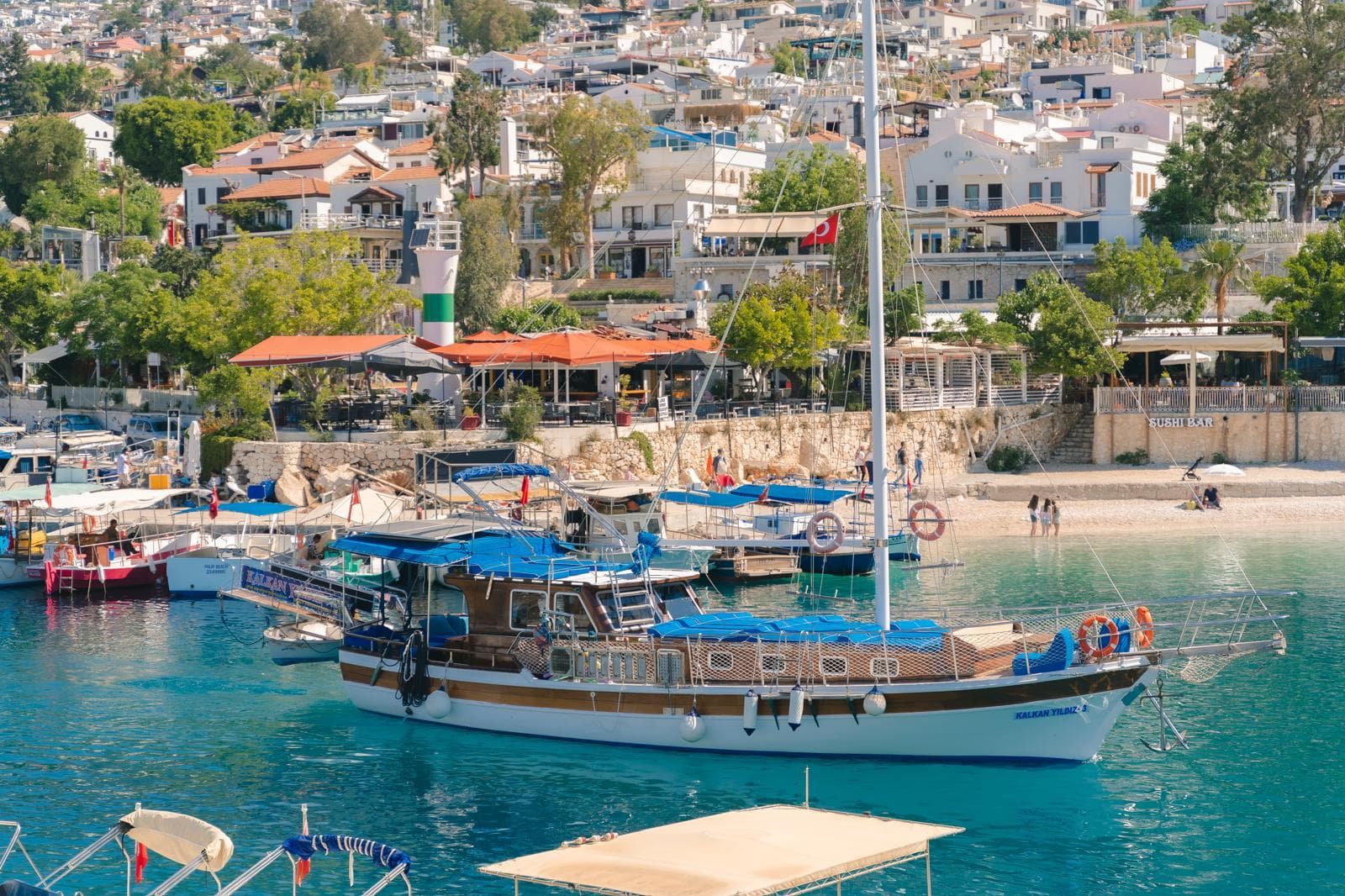 A traditional wooden gulet moored in Kalkan harbour, with the town's whitewashed hillside houses rising behind it