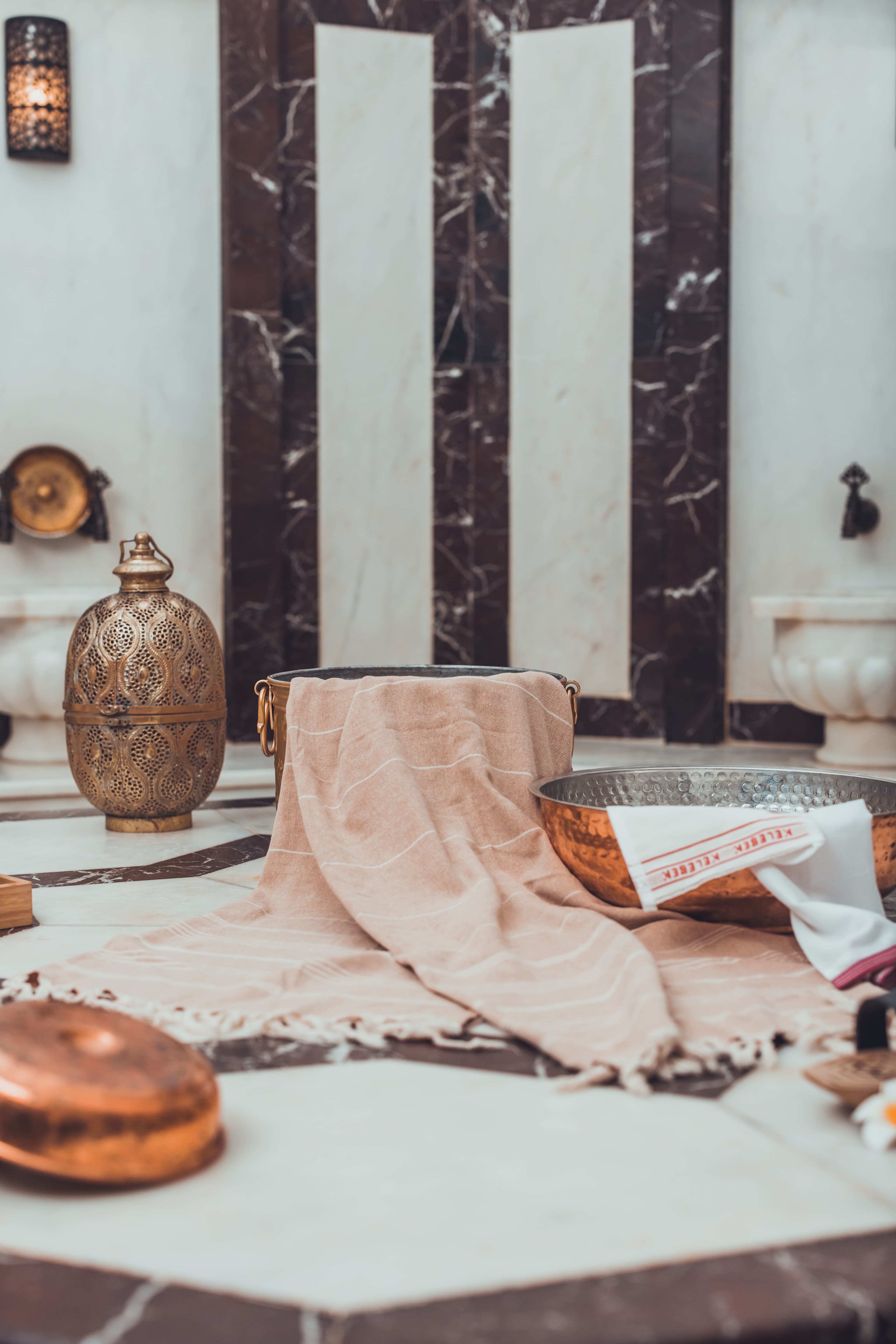 A Turkish hammam interior with marble surfaces, copper bowls, and a folded pestemal towel