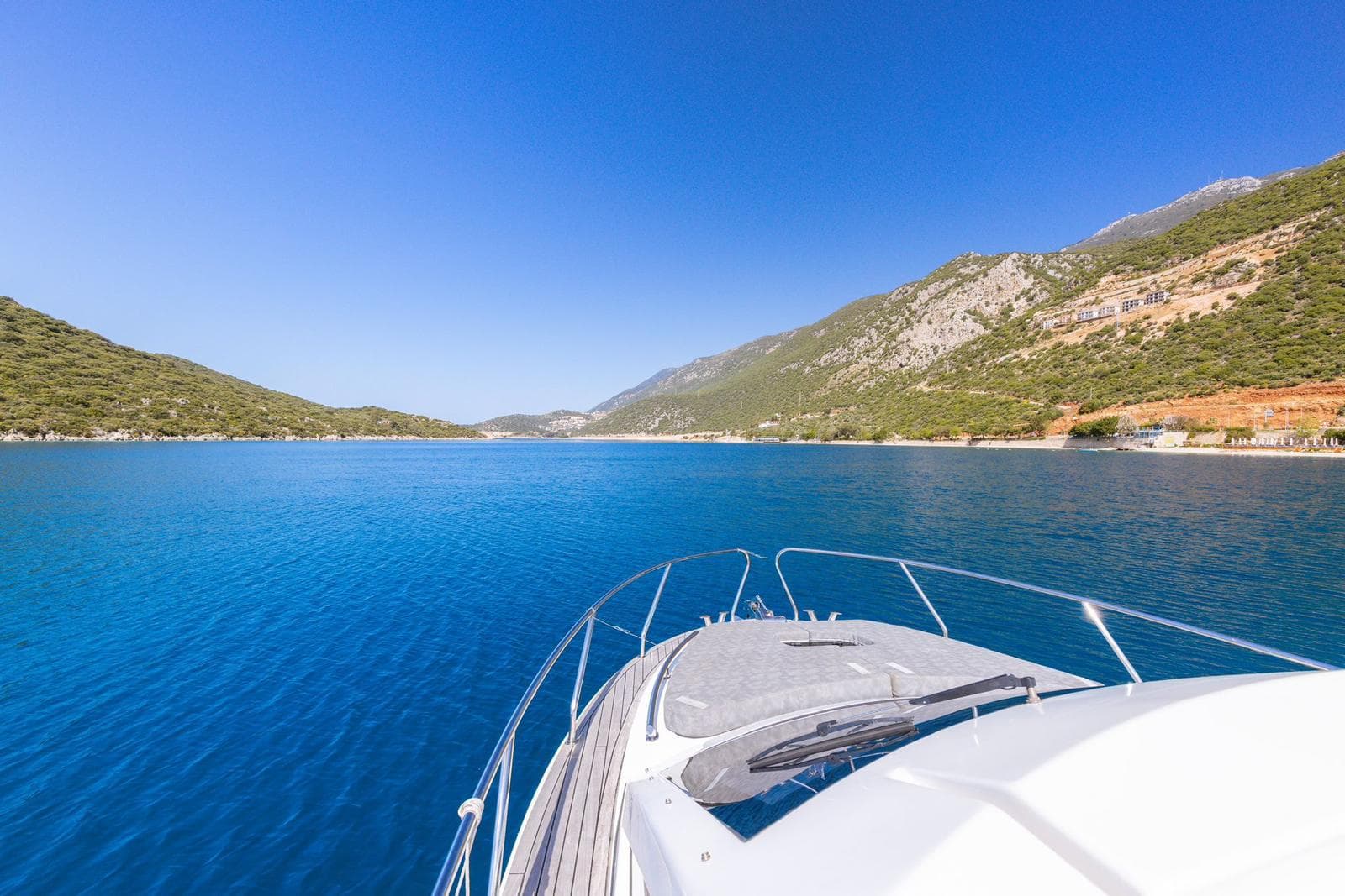 The view forward from a yacht's bow across a turquoise Mediterranean bay toward the Kaş coastline