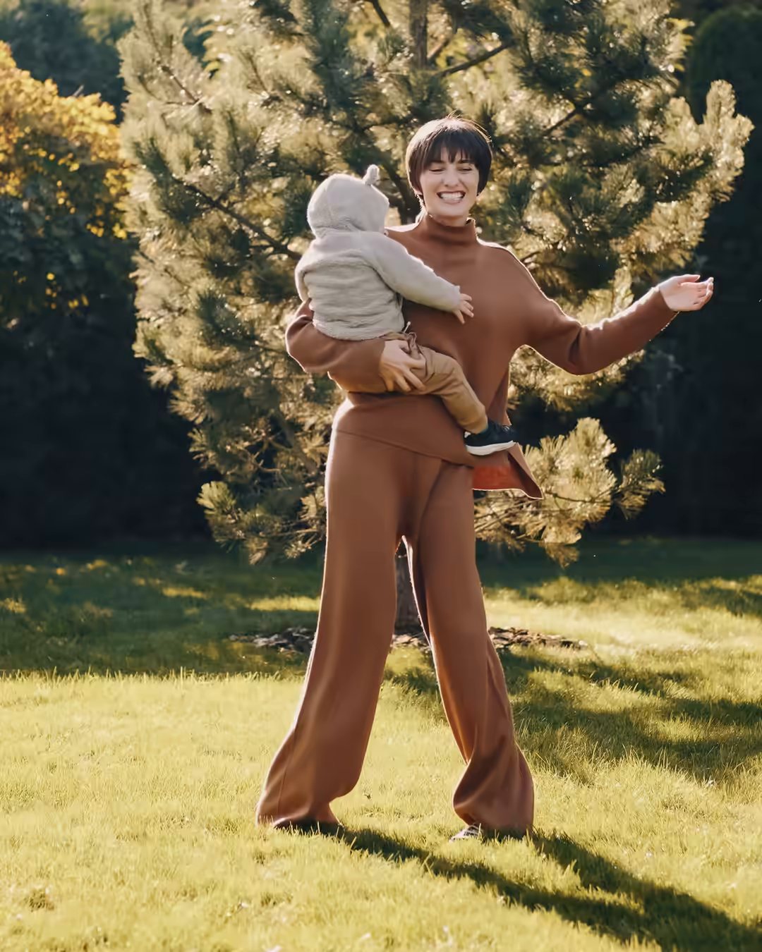An adult holding a small child on a sunlit garden lawn