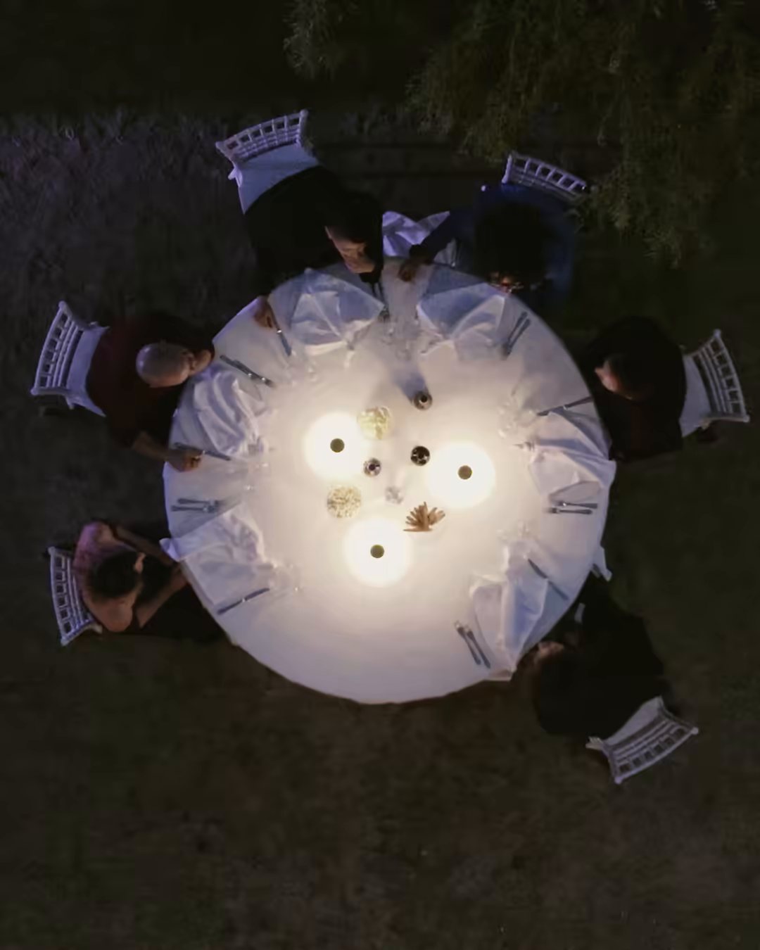 A round dinner table lit at night, seen from above